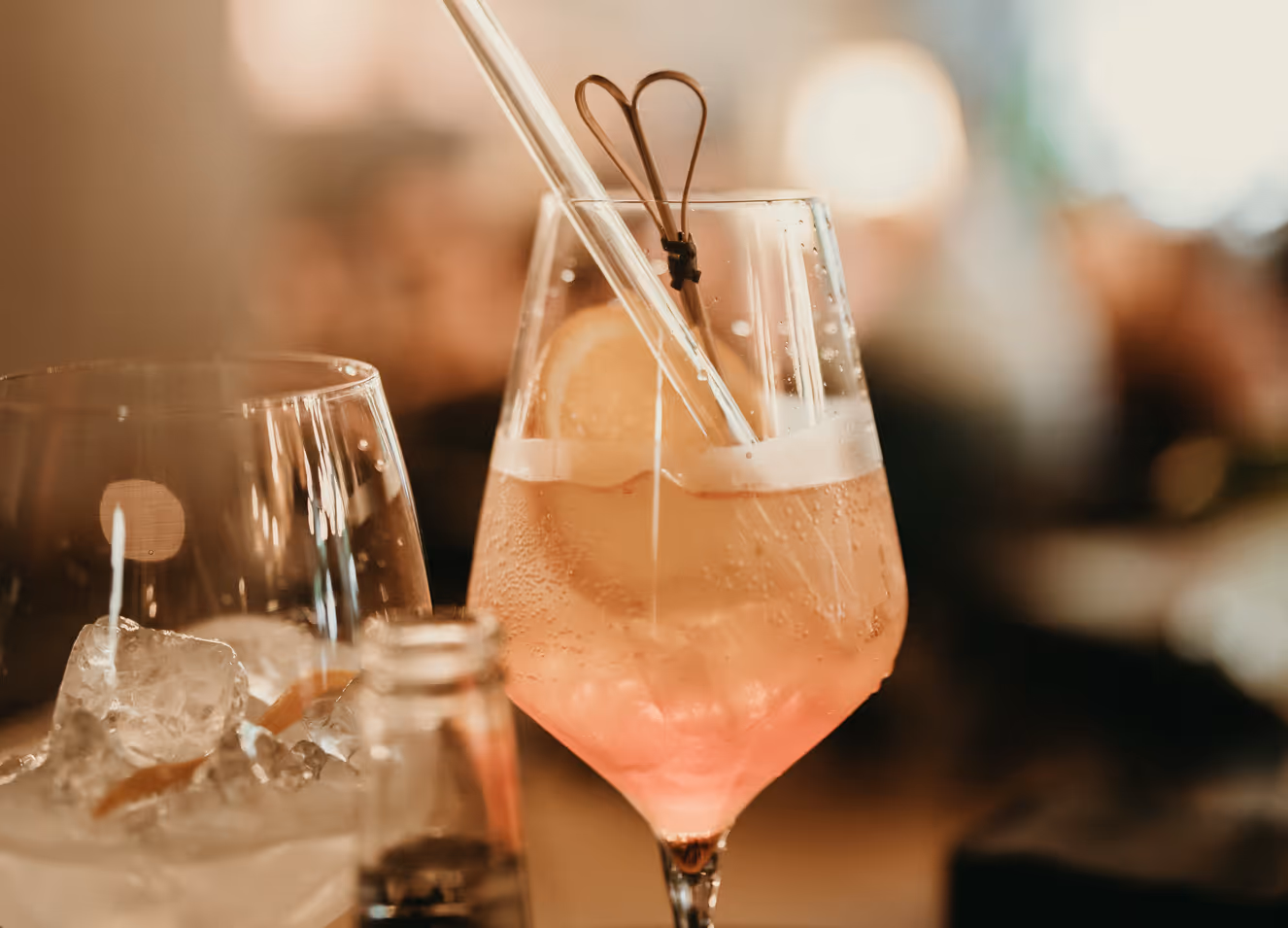 Glas mit einem erfrischenden pinken Cocktail, Eiswürfeln, Zitronenscheibe und einem Herz-förmigen Rührstab.